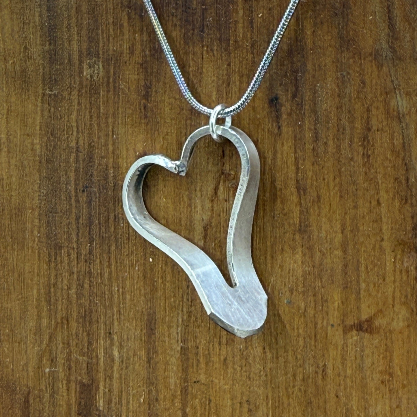 Heart-shaped silver pendant on a chain against a wooden background