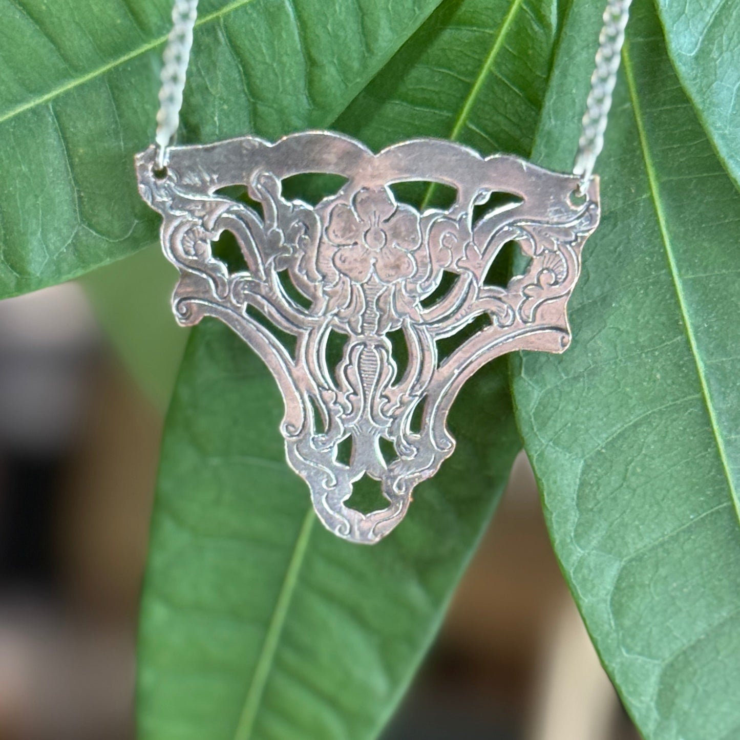 Silver necklace with a detailed pendant against green leaves