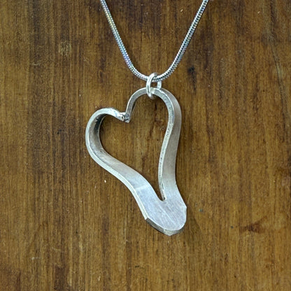 Heart-shaped silver pendant on a chain against a wooden background