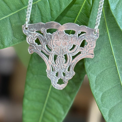 Silver necklace with a detailed pendant against green leaves